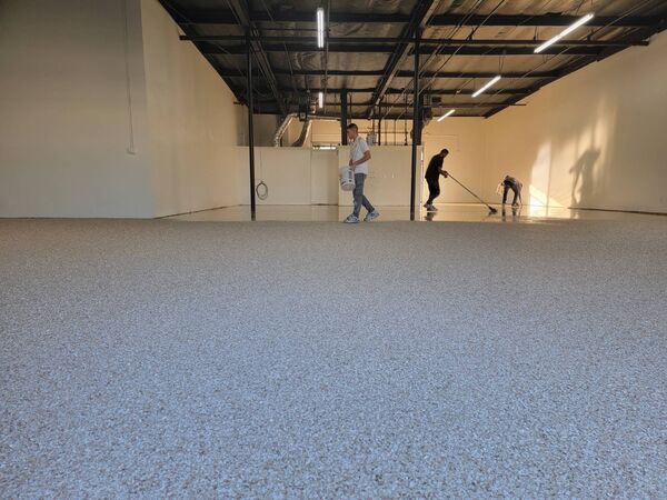 Large commercial warehouse floor with gray decorative flake epoxy coating and installation crew